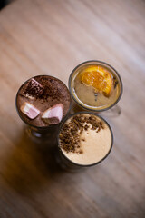
cocoa with marshmallows, tea with orange, raf with peanuts in glass irish glasses on a wooden table top view.