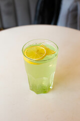 green lemonade with lemon in a glass glass on a white table with a blurred gray background.