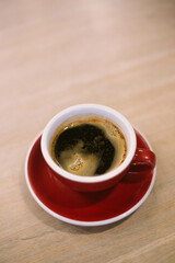 americano in a red ceramic cup on a saucer on a wooden table from above.
