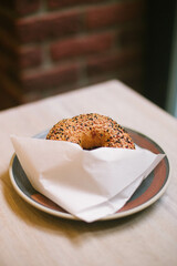 Bagel on a wooden table in a paper envelope, on a plate in a paper envelope on a wooden table against a brick wall.