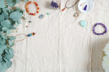 Backdrop or Flat lay background of raw stone and crystal, i.e. Amethyst, Amazonite, kayanite, 7chakra pendant and incense on linen cloth, green eucalyptus and white flower with copy space in daylight.