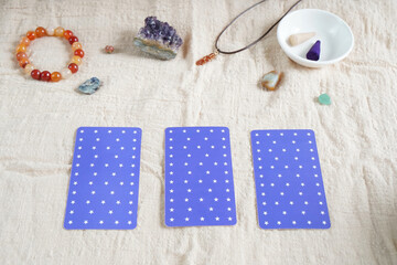 Flat lay of purple tarot card on linen fabric decor with crystal, stone, and white flower incense in daylight. Reading fortune pass through pick a card by gypsy. Many type in arrange card to forecast.