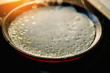 Pancake is baked in black cast iron skillet and there is smoke. Preparation of delicious traditional dessert at home. Aromatic pastries.