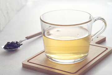 Green tea (Chinese milk oolong) in a transparent mug on the table. Behind lies a teaspoon with tea leaves. Rest