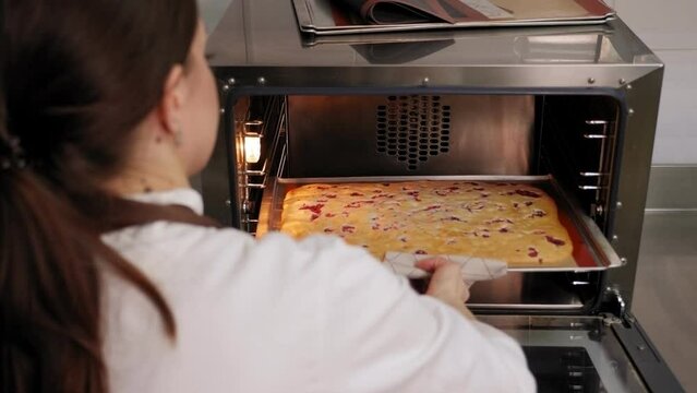 Close-up of a female cook takes out a baking sheet with bikwit from a baking oven. The pastry chef prepares a sweet delicious cake in a professional kitchen.