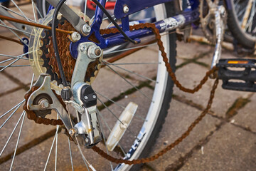 Blue bike has been outside all winter and got broken. Rusty bicycle chain hangs on sprocket and gear.