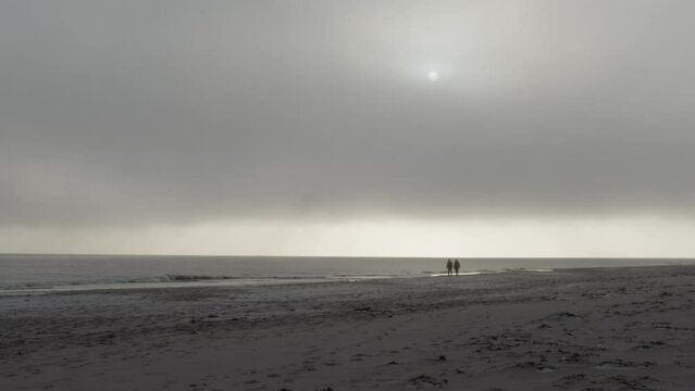 Couple in distant walking on a beach on a foggy Scandinavian day in slow motion and 4K.