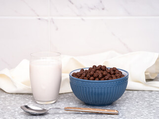 A bowl with chocolate cereal and a glass of milk on a table
