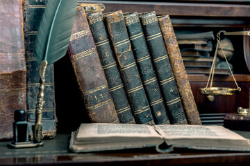 Old quill pen, books and vintage inkwell on wooden desk in the old office against the background of...