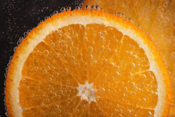 Slice of orange fruit in water with gas bubbles. Refreshing citrus drink, cocktail.