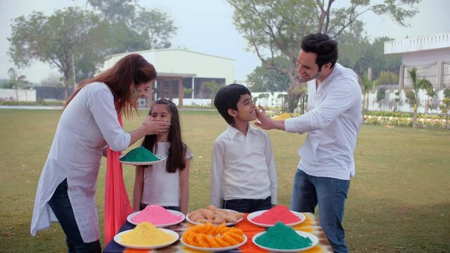 A happy young couple celebrating Holi together with their son and daughter - an Indian festival  Holi party  Indian family celebrating holi. Adorable brother-sister with colorful faces posing for t...