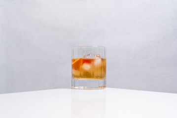 Vaso de vermut rojo con hielo decorado con cerezas y rodajas de naranja sobre mesa blanca	