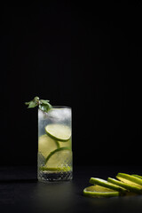 Un vaso de ginebra y tónica con rodajas de lima y hielo sobre fondo negro	