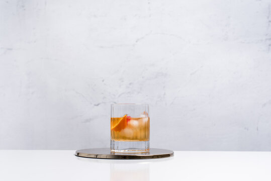 Vaso de vermut rojo con hielo decorado con cerezas y rodajas de naranja sobre mesa blanca	