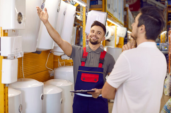 Young man at the store looking at modern electric water heaters and thinking. Friendly salesman showing a customer a wide range of thermodynamic boilers and wall water heaters for bathroom and kitchen
