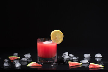 Un vaso de refrescante jugo de sandía triturado adornado con trozos de sandía sobre hielo picado. Cóctel de frutas en fondo negro