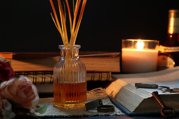 aroma scented reed diffuser bottle or air freshener is on wooden table with a few books , old keys , rings and rose flowers in the living room of the house to creat relax ambient for reading book