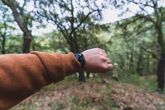 Vista en primera persona de brazo con reloj con fondo de bosque en la subida de ruta verde