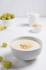 Crema de almendras, sopa fría española. Ajo blanco de Málaga con almendras y uvas en un recipiente blanco sobre una mesa blanca	