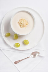 Crema de almendras, sopa fría española. Ajo blanco de Málaga con almendras y uvas en un recipiente blanco sobre una mesa blanca. Vista superior	