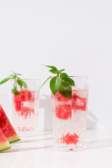 Dos vasos de zumo de sandía con hojas verdes trozos de sandia y hielo sobre fondo claro