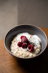 Healthy breakfast oatmeal porridge with yogurt and frozen raspberries in bowl. Warm porridge oats, vegan vegetarian weight loss dieting breakfast food