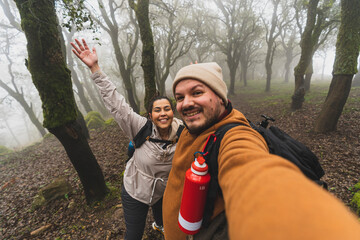 Selfie de una pareja joven en un bosque haciendo senderismo con niebla por los arboles