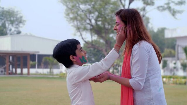 A pretty female and a young boy smearing each other's faces with powder colors - Holi festival celebrations  vibrant colors. An affectionate mother embracing her sweet son lovingly while celebratin...