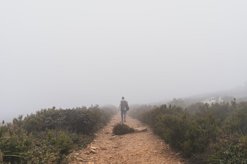 Obraz premium Chico joven bajito andando por camino de piedra rodeado de niebla y tomando fotos