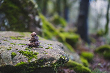 Apilamiento de piedras sobre roca grande con musgo en mitad de un bosque con niebla