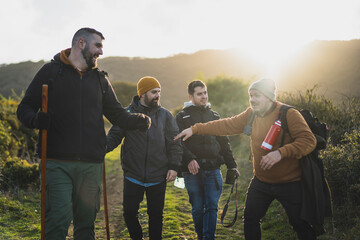 Fototapeta premium Grupo de amigos en ruta verde con el sol y las montañas de fondo mientras sonrien 
