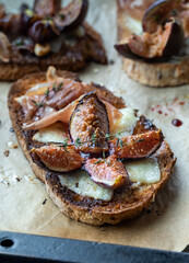 Toasted fig and prosciutto tartines on a parchment lined baking sheet.