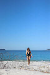 walking young woman in bikini and sunglasses on beach