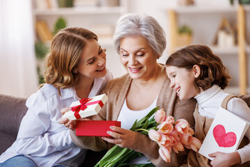 Happy International Women's Day.Smiling  daughter and granddaughter giving flowers  and gift to grandmother   celebrate spring holiday Mother's Day at home