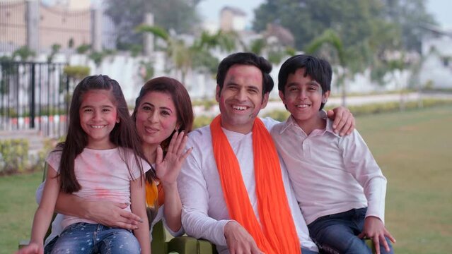 A modern Indian family wishes a Happy Holi to everyone on a video call - an Indian festival  family bonding. A young couple and little kids waving their hands while chatting online - distant commun...