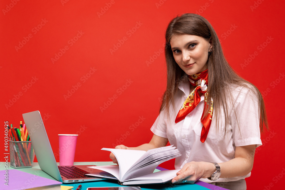 Wall mural A young woman in a white shirt writes down plans in a diary on a red background