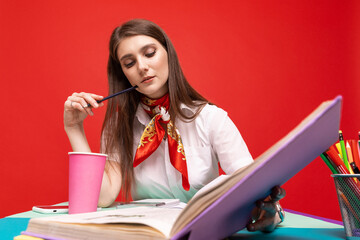 A young woman in a white shirt works at a desk on a red background