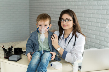 .Medical doctor applying medicine inhalation treatment on a little boy with asthma inhalation therapy by the mask of inhaler. - obrazy, fototapety, plakaty