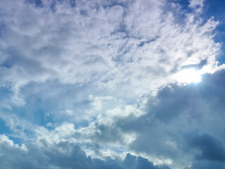 Bright cloudscape, with the bottom half of darker fluffy cumulus clouds giving way to high feathery cirrus as the sun bursts between.