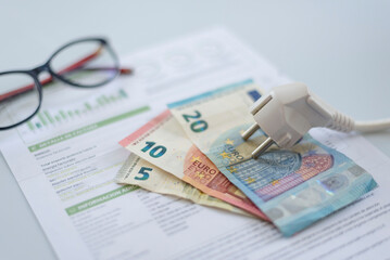 a white electric cap, euro bills and a pair of glasses on an electric bill, . Rising cost of...