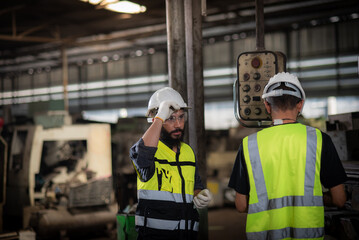 A new worker, latin mix race man worker have unkempt beard in safety uniform is being training on the job or coaching from a supervisor to control the heavy machine in industrial manufacturer factory.