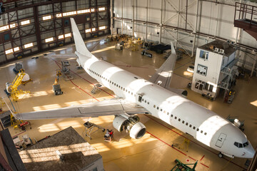 Top view of a white passenger airplane in the hangar. Aircraft under maintenance. Checking mechanical systems for flight operations - obrazy, fototapety, plakaty