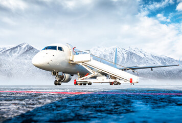 White passenger airplane with air-stairs at the airport apron on the background of high scenic mountains
