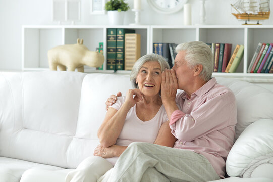 Senior couple sitting on sofa at home sharing secret