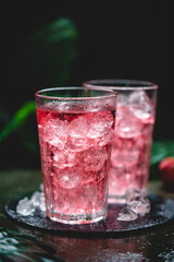 Red drink cocktail or lemonade with ice in a glass on dark background.