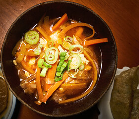 Wooden bowl of Japanese miso soup with a vegetable garnish of carrots, onions, leeks and green onions