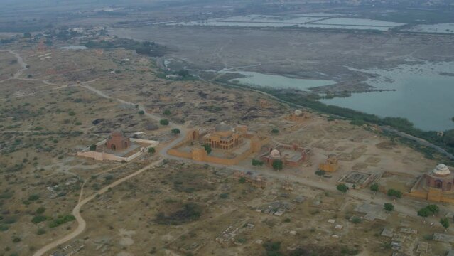 Aerial drone shot over Tomb of Dewan Shurfa Khan on Makli Hill beside a lake on a sunny day in Thatta, Pakistan 