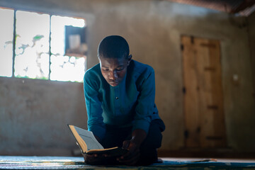 African teenage boy sitting and reading book in poor school, high quality photo