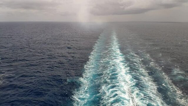 Still shot from rear of a cruiser. Mediterranean sea horizon with clouds. Water propulsion trail can be seen on the water and steam from the boats engine leaving smoke behind.