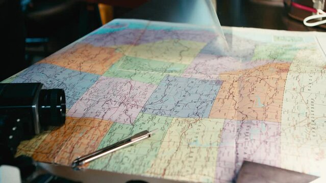 A man's hand turns a paper map of the world. He puts it on the table and looks for a place on the map.